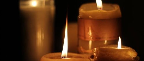 Vier Kerzen sind in einem schwach beleuchteten Bereich angezündet. Die Kerzen variieren in Größe und Form. Die Flamme jeder Kerze ist hell und erhellend.