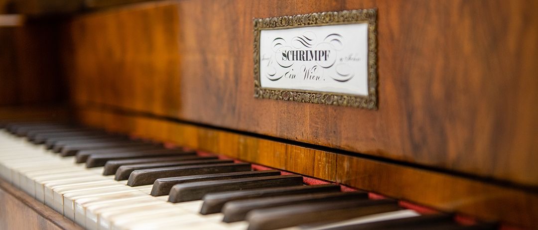 Ein Nahaufnahme eines Vintage-Pianos mit einem Namensschild, das 'SCHRIMPI in Wien' zeigt, mit elegantem Holzdesign und gut erhaltenen Tasten.