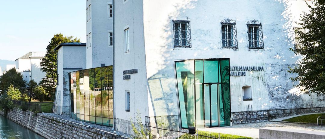 Ein weißes Gebäude mit vielen Fenstern steht am Ufer eines Kanals. Es hat einen modernen Glaseingang.