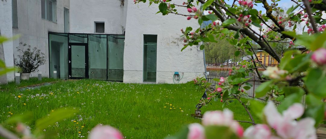Ein Gebäude mit Glastüren und Fenstern, umgeben von einem grünen Rasen mit blühenden Apfelbäumen.
