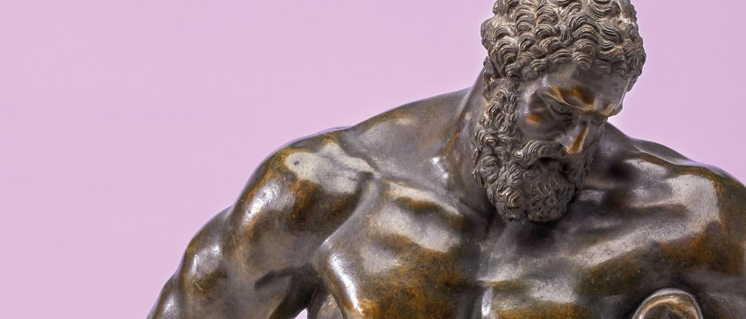 Eine Bronzestatue eines bärtigen Mannes mit muskulöser Statur, der mit einer Hand auf der Hüfte und der anderen Hand, die einen Schild hält, steht.