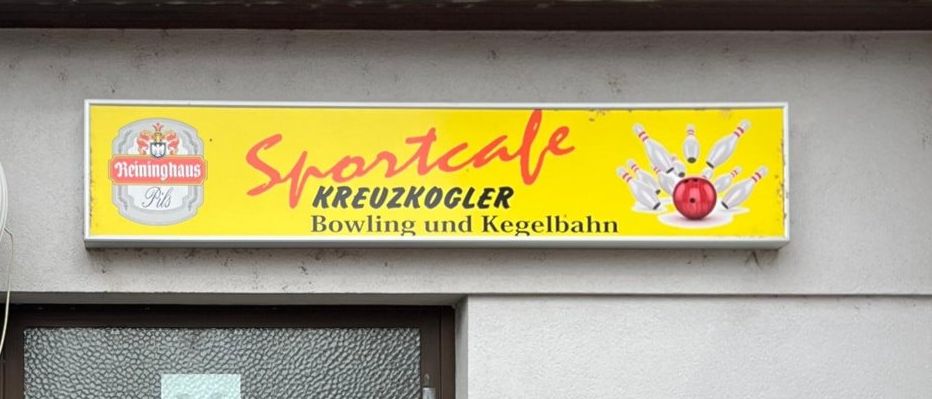 Eine Gruppe von Frauen steht vor einer Bowlingbahn. Das Schild über dem Eingang lautet Sportcafe Kreuzkogler Bowling und Kegelnbahn.