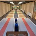Kegelbahn mit leeren Bahnen und einer digitalen Anzeigetafel. Die Bahnen haben rote Linien an der Seite, und ein blauer Bowlingball befindet sich auf der Bahn.