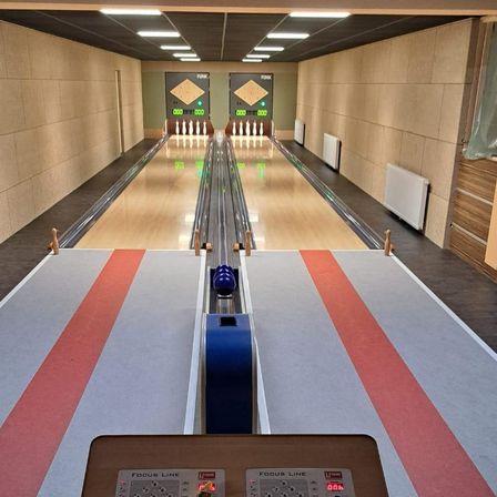Kegelbahn mit leeren Bahnen und einer digitalen Anzeigetafel. Die Bahnen haben rote Linien an der Seite, und ein blauer Bowlingball befindet sich auf der Bahn.