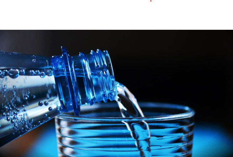 Eine Flasche Wasser wird auf einen schwarzen Hintergrund in ein Glas gegossen. Das Wasser und das Glas haben einen blauen Schimmer.