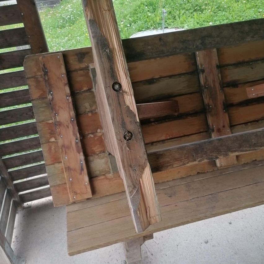 Nahaufnahme einer Holzbank mit sichtbaren Schrauben und Holzbrettern, auf dem Rasen eines Gartens.