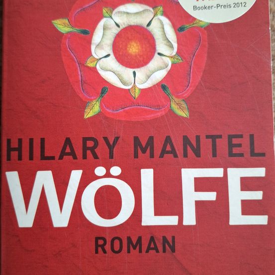 Ein roter Buchdeckel mit einer weißen Rose in der Mitte, 'Wölfe' in weißer Schrift und 'Roman' darunter. 'Booker-Preis 2012' oben.