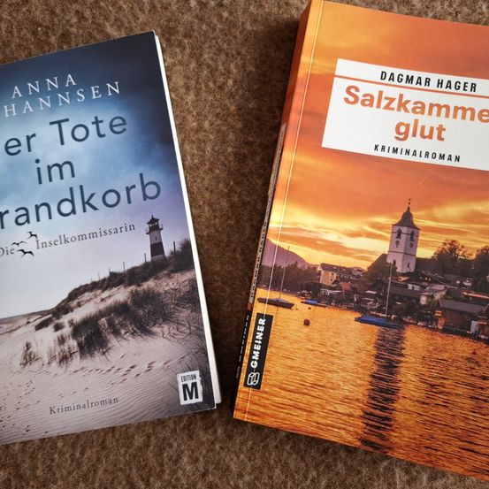 Zwei Kriminalromane nebeneinander. Das linke Buch hat einen blauen Umschlag mit dem Titel 'Anna Hansen'. Das rechte Buch hat einen orangefarbenen Umschlag mit dem Titel 'Salzkammergut' von Dagmar Hager.