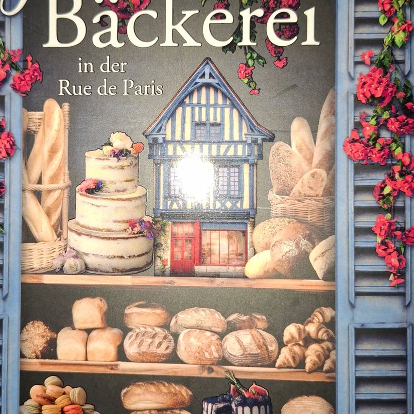 Eine Illustration eines Bäckereiladens zeigt verschiedene Brote, Kuchen und Gebäck auf Regalen. Über den Regalen befindet sich ein Kuchen mit Blumen, ein Korb mit Brot und ein traditionelles Haus. Der Text lautet 'Backerei in der Rue de Paris.'