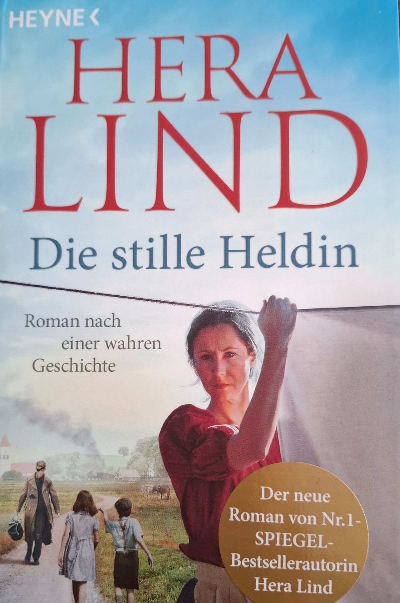 Book cover titled 'LIND' featuring a woman in a red dress holding a white cloth, with a man in a coat standing behind her. The background shows a rural scene with a church and a field.