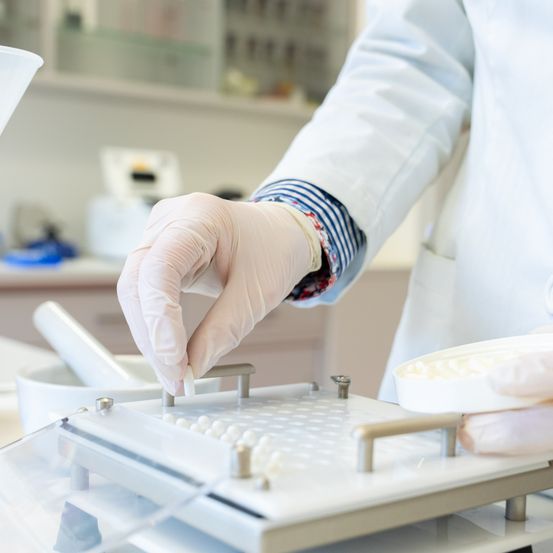 Eine Person in Laborkittel und Handschuhen greift nach kleinen weißen Perlen auf einem Labortablett.