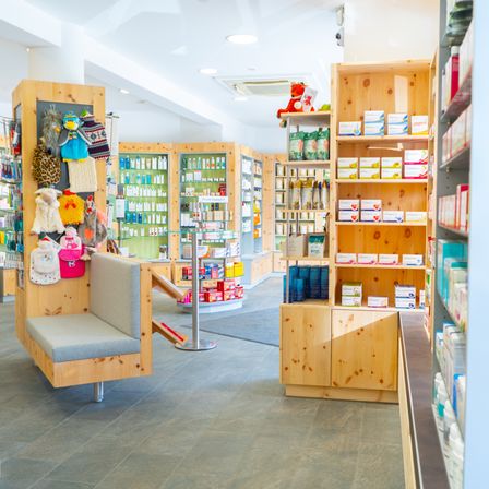 Innenbereich einer Apotheke mit Holzregalen, Spielzeug und Produkten ordentlich organisiert und einer Bank in der Ecke.