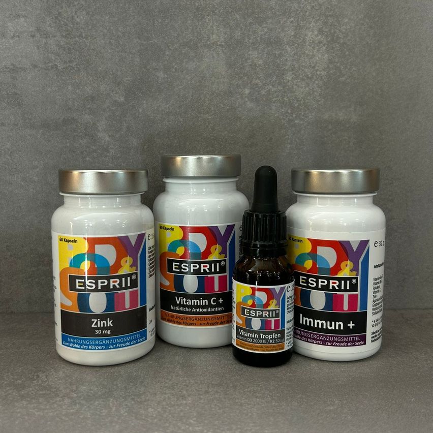 Vier Gesundheitsergänzungsflaschen sind ausgestellt. Eine Flasche ist mit Zink beschriftet, eine andere mit Vitamin C+, die dritte mit Vitamin Tropfen und die vierte mit Immun+. Jede Flasche hat ein einzigartiges Farbschema und Etikettendesign.