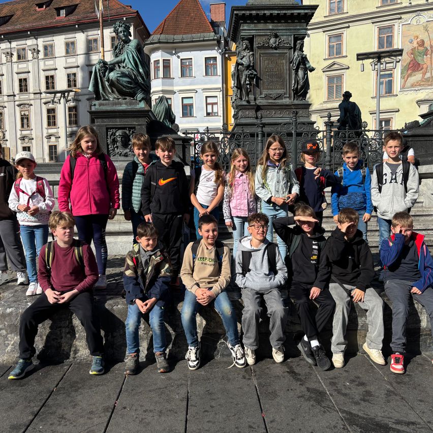Eine Gruppe von Kindern und Jugendlichen posiert für ein Foto vor einem Denkmal in einer europäischen Stadt.