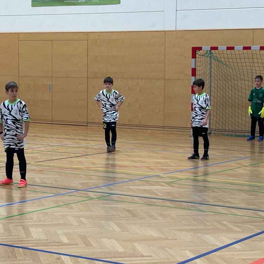 Fünf Jungen stehen auf einem Basketballplatz, alle tragen identische Trikots mit Zebrastreifen. Der Platz hat ein Tor und blaue Markierungen.