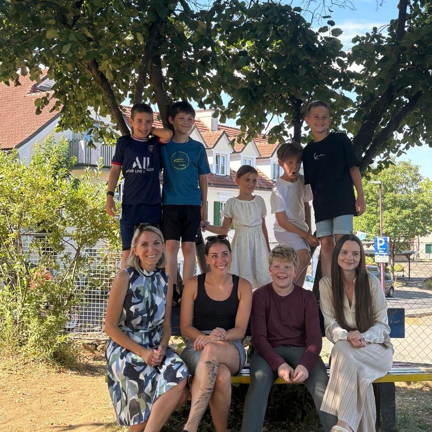 Eine Gruppe von Menschen, einschließlich Erwachsener und Kinder, posiert für ein Foto unter einem Baum in einem Park.