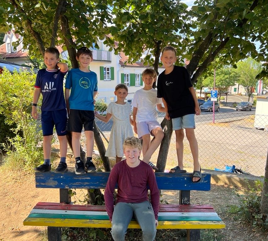 Eine Gruppe von Kindern, einige stehen auf einer Bank und andere lehnen sich an einen Baum, posiert für ein Foto im Park.