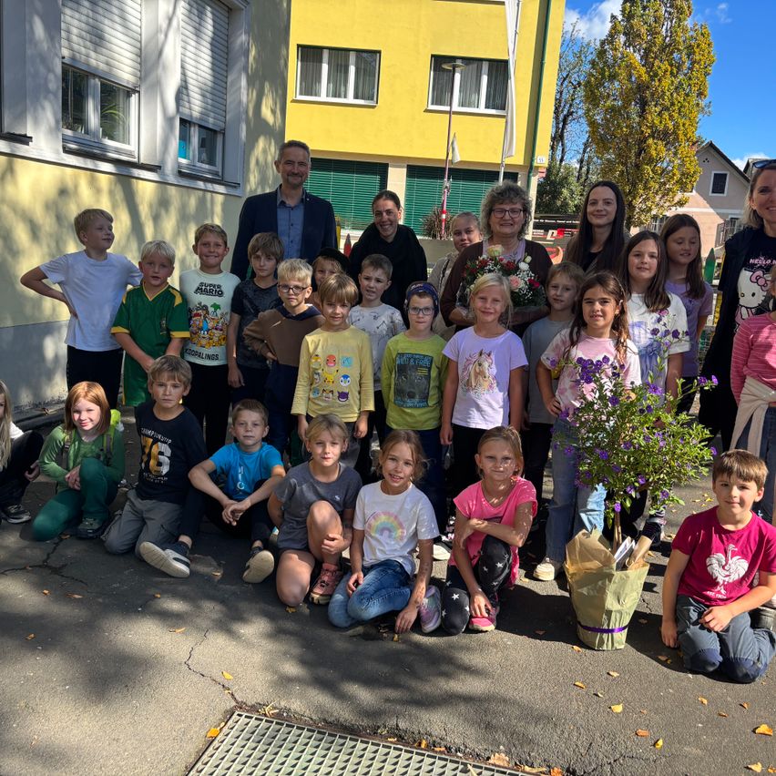 Eine Gruppe von Kindern und Erwachsenen posiert für ein Foto vor einem gelben Gebäude. Einige Kinder halten Blumen.