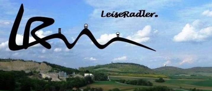 Eine szenische Luftaufnahme von sanften Hügeln unter einem bewölkten Himmel mit 'LeiseRadler' im Vordergrund. Die Landschaft zeigt saftige grüne Felder und ein entferntes Dorf.