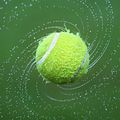 Ein Tennisball dreht sich in der Luft, umgeben von Wassertropfen vor einem leuchtend grünen Hintergrund.