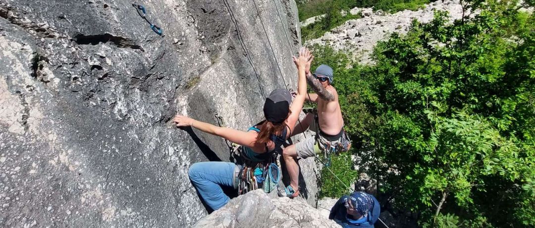 Zwei Kletterer erklimmen einen felsigen Abhang, einer mit Tätowierung, der andere mit Bandana. Ein dritter Kletterer ist darunter.