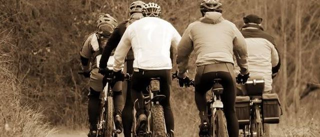 Eine Gruppe von Radfahrern fährt zusammen auf einem Pfad mit Bäumen an den Seiten und trägt Helme und Handschuhe.