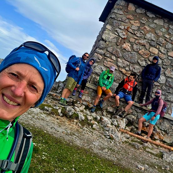 Eine Gruppe von Wanderern posiert vor einer Steinstruktur auf einem Berg.