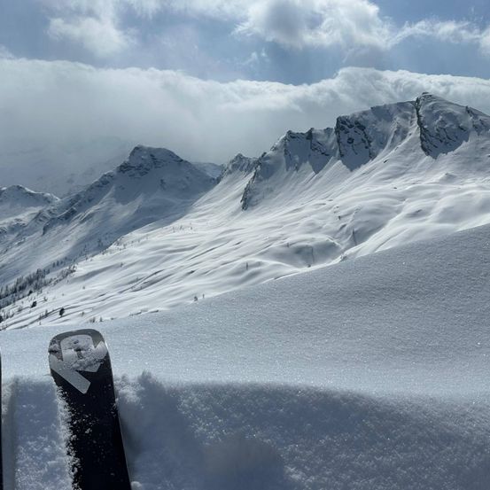 Ein verschneiter Berg mit einem Ski, der zur Hälfte im Schnee vergraben ist, im Vordergrund.