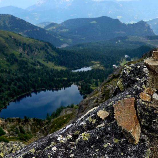 Ein Blick aus großer Höhe auf einen ruhigen See, umgeben von üppigem grünem Wald und felsigen Bergen.
