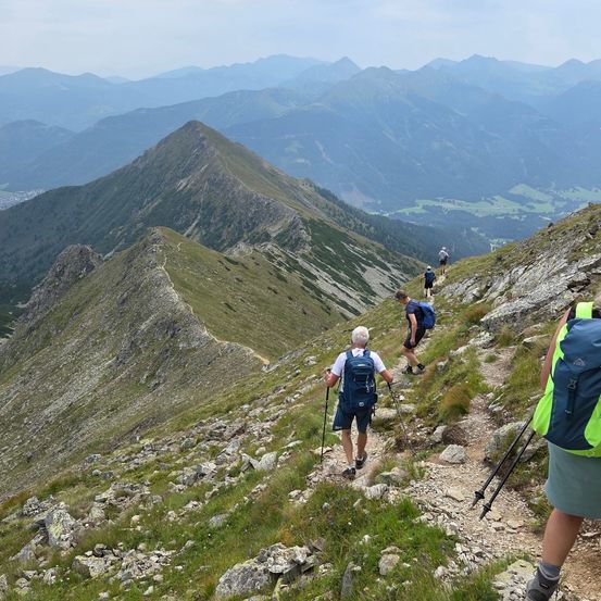 Eine Gruppe von Wanderern erklimmt einen felsigen Bergpfad, mit einer bergigen Landschaft im Hintergrund.