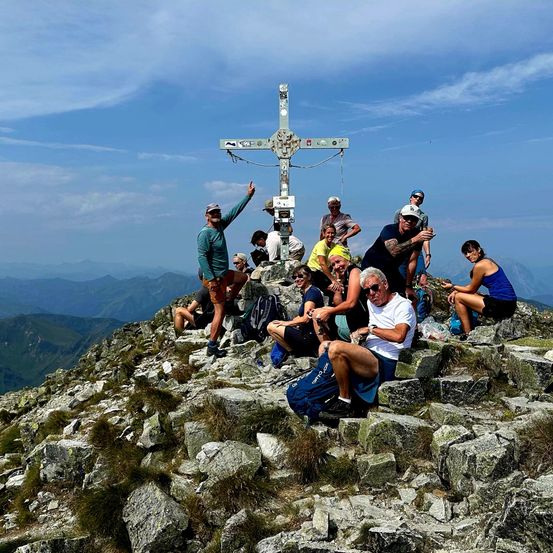 Eine Gruppe von Wanderern posiert für ein Foto auf dem Gipfel eines Berges, mit einem großen Kreuz im Hintergrund.