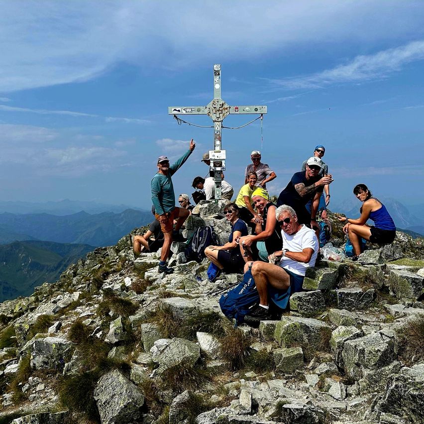 Eine Gruppe von Wanderern posiert für ein Foto auf einem Berggipfel mit einem Kreuz im Hintergrund.
