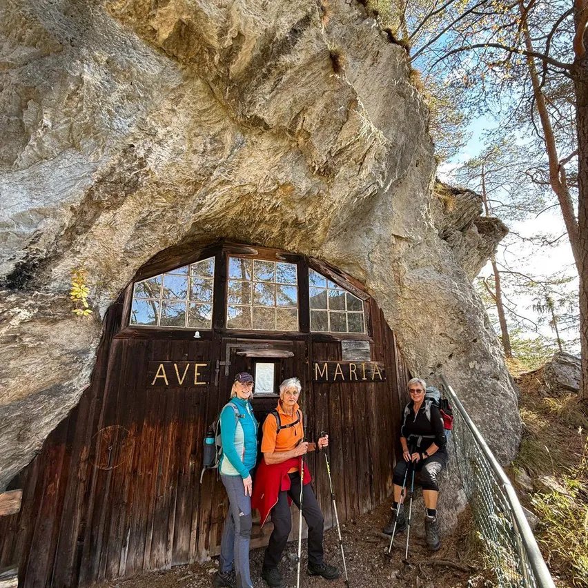Drei Wanderer stehen vor einer in einen Fels eingelassenen Holztür, mit den Worten Ave Maria darauf.