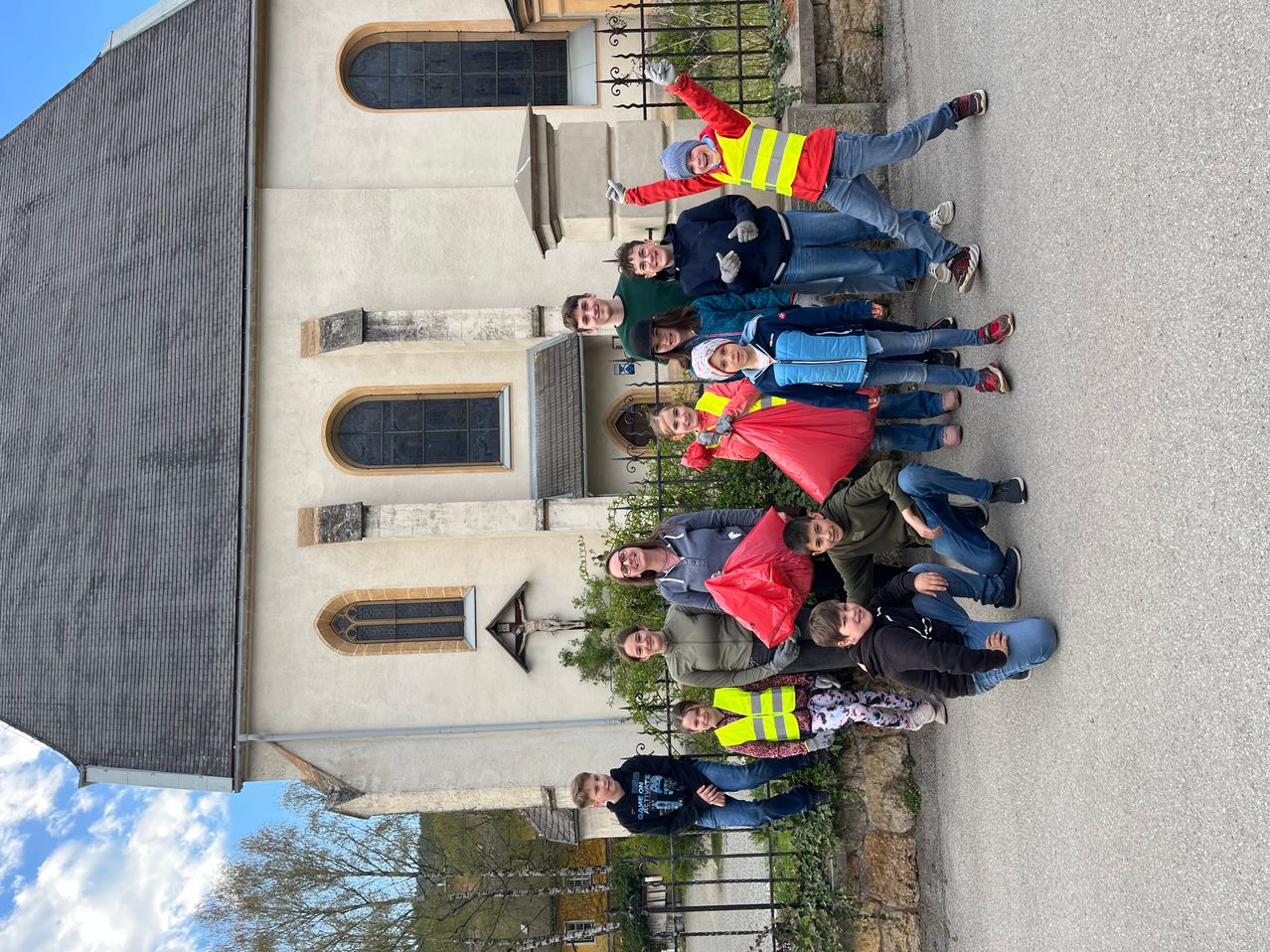 Eine Gruppe von Menschen in Warnwesten und mit Taschen posiert für ein Foto vor einer Kirche.