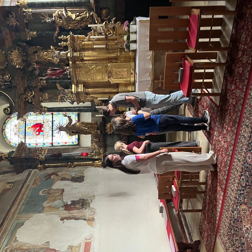 A group of people, dressed in casual attire, are observing a golden altar and ornate wall decorations inside a church.