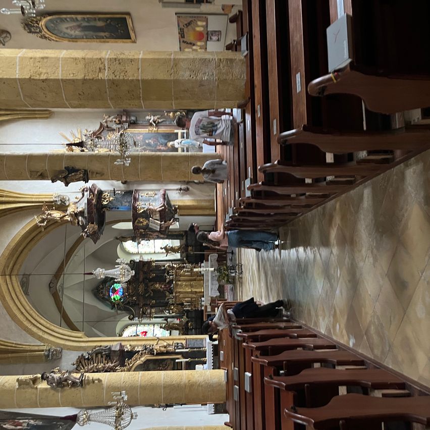 Aerial view of a church interior with wooden pews, ornate pillars, and various statues and decorations, with people cleaning and arranging the area.