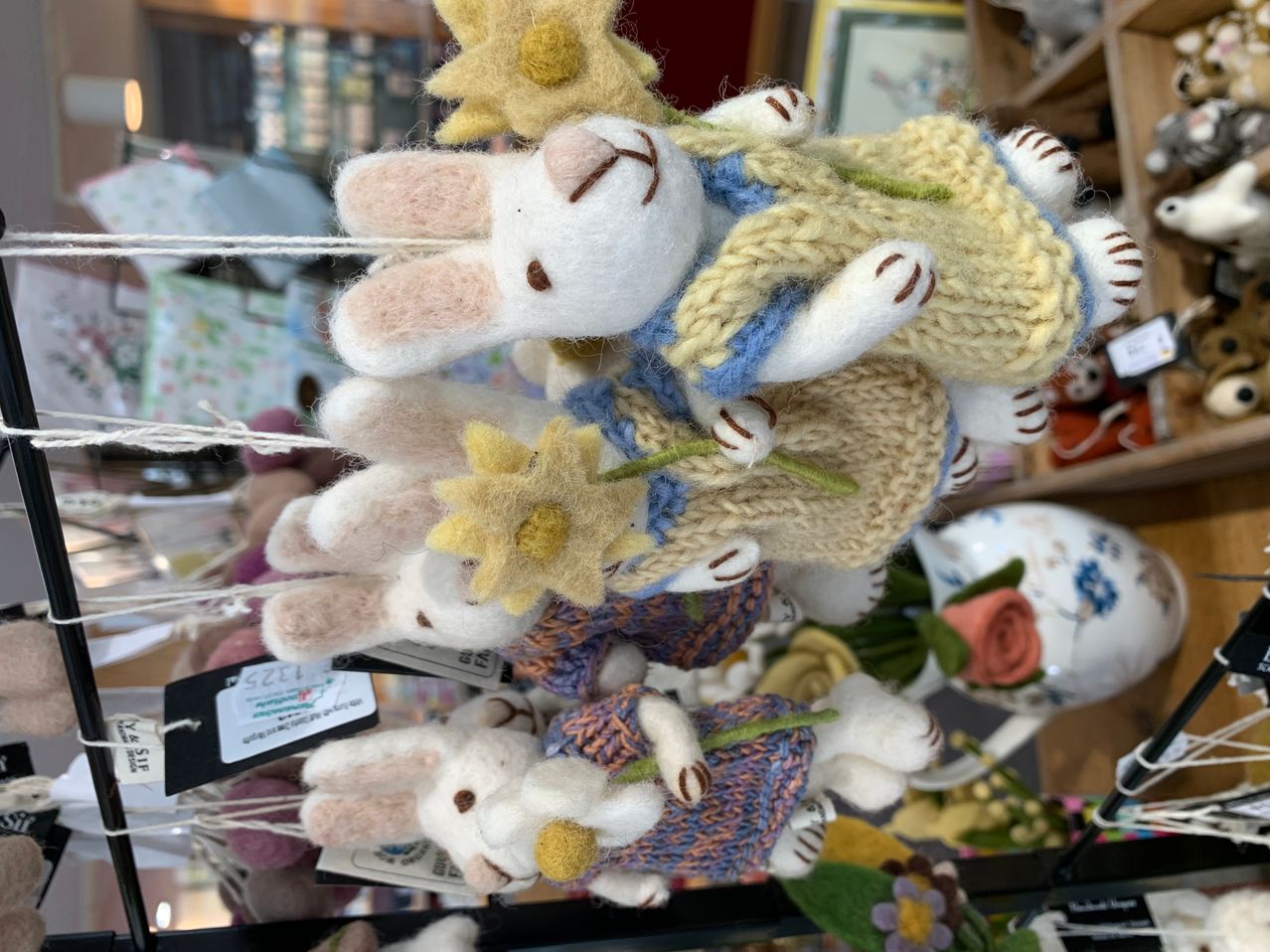 Vier handgefertigte Stoffhasen mit gestrickten Kleidern und Blumen hängen an einer Schnur. Die Hasen sind aus Wolle und haben verschiedene Farben.