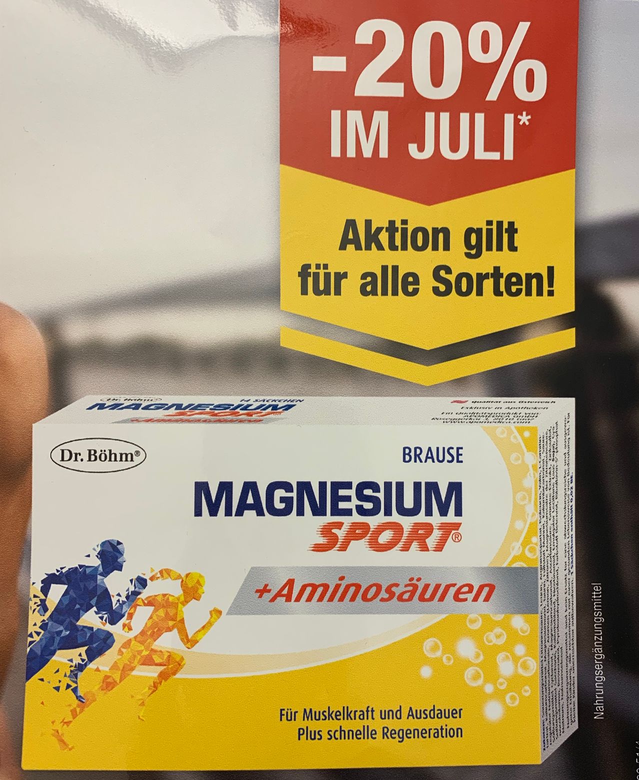 Eine Schachtel Magnesium Sport Tabletten wird mit einer Aktion von 20% Rabatt im Juli gezeigt. Die Tabletten sind blau und orange mit einer rennenden Figur.