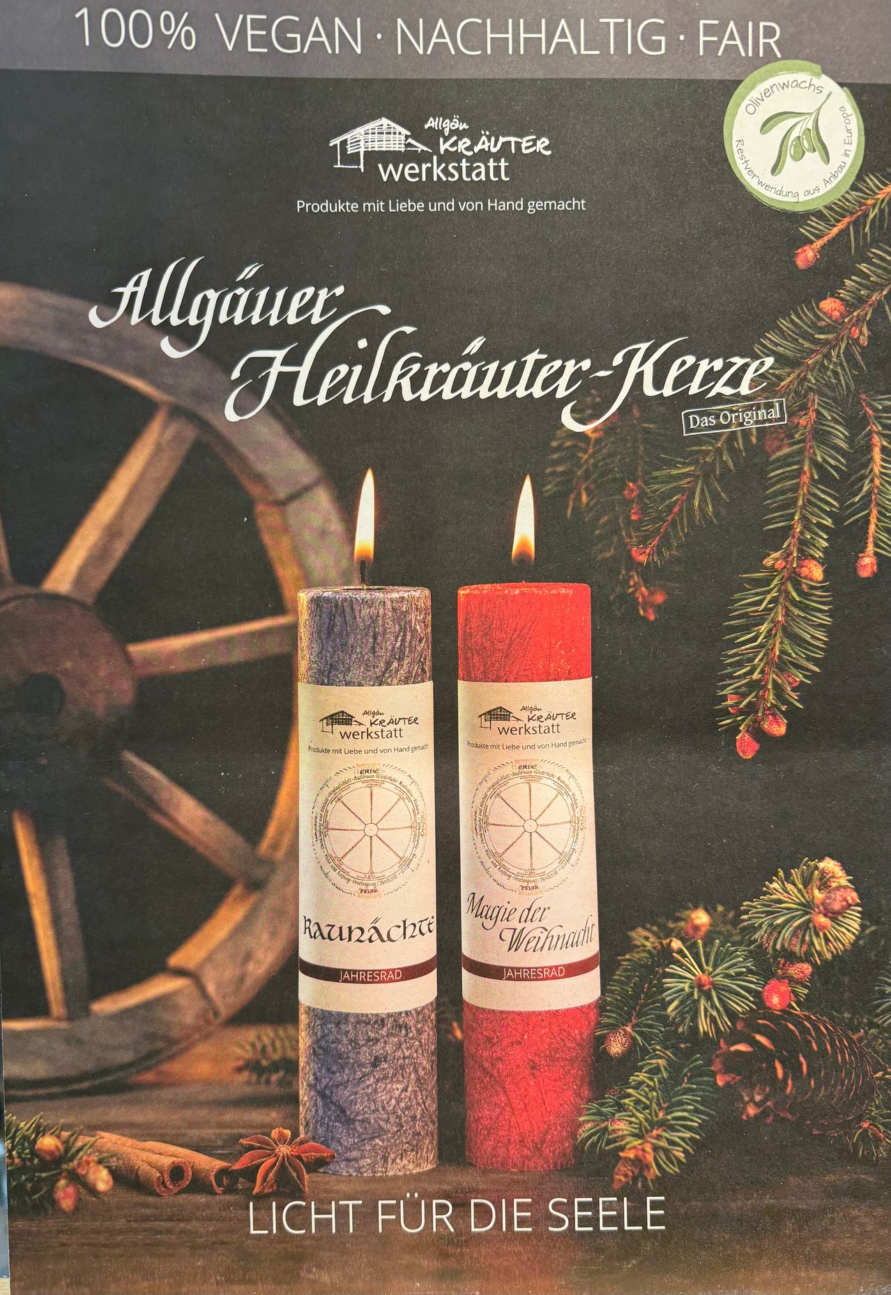Zwei handgemachte Kerzen vor einem Rad und einem Weihnachtskranz. Die Kerzen sind rot und lila mit deutschen Etiketten. Der Hintergrund ist dunkel.