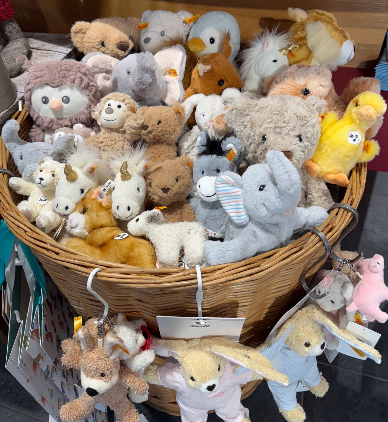 A large wicker basket filled with various stuffed animals, including bears, elephants, and unicorns, is displayed. Some animals have tags attached.