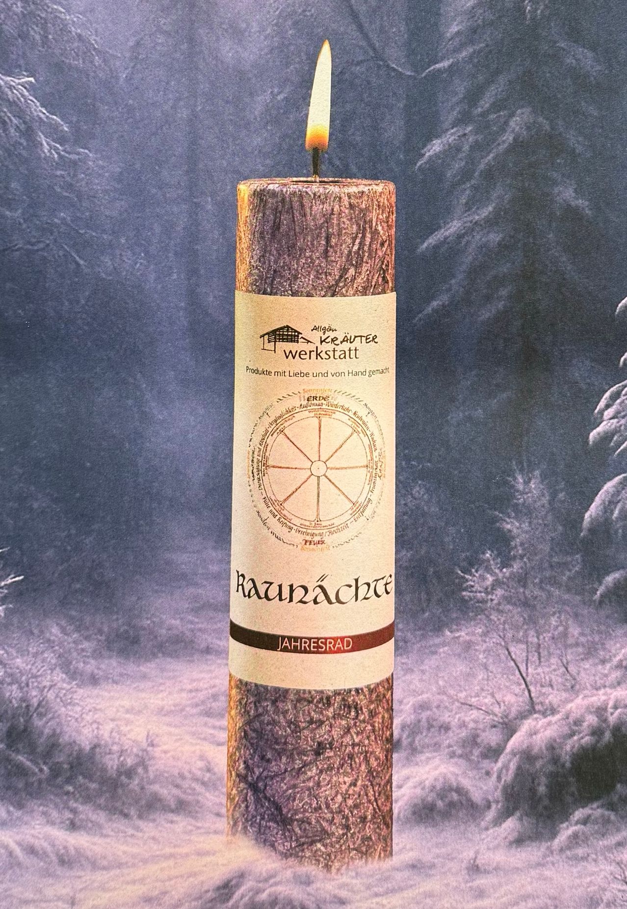 Eine große Holzkerze mit einem Etikett, das 'Raunächte' und 'Jahresrad' zeigt, ist zu sehen. Das Etikett hat auch ein Logo und ein Raddesign. Der Hintergrund ist verschwommen mit verschneiten Bäumen.