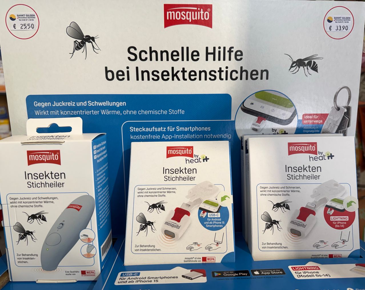 Drei Schachteln von Mückenschutzgeräten sind ausgestellt. Die oberste Schachtel hat einen blauen Hintergrund mit Text über schnelle Linderung von Insektenstichen. Die mittlere Schachtel zeigt ein Gerät mit einem USB-C-Anschluss für Android und iPhone 15. Die unterste Schachtel hat ein ähnliches Design mit einem USB-C-Anschluss.
