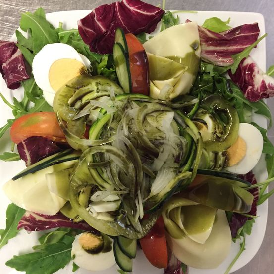 Ein Teller mit Salat mit Artischocken, Gurken, Eiern und verschiedenen Gemüsesorten. Der Salat ist mit roten Radicchioblättern garniert und mit Dressing beträufelt.