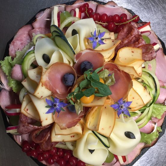 Ein Teller mit verschiedenen geschnittenen Fleischsorten, Käse, Gemüse und Beeren, garniert mit Blumen und Kräutern.