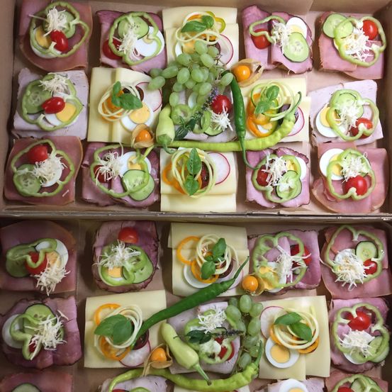 Eine Schachtel enthält eine Auswahl an Sandwiches mit verschiedenen Belägen wie Käse, Eiern, Tomaten und Paprika. Einige Sandwiches haben grüne Paprika in Herzform.
