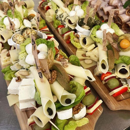 Mehrere Holzplatten halten eine Auswahl an Käse, Oliven und anderen Zutaten. Jede Platte ist mit Blättern und verschiedenen Toppings verziert, einige mit Zahnstochern.