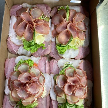 Eine Schachtel mit sechs Sandwiches, jedes belegt mit Schinken-, Käse- und Salatblättern.