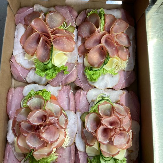 Eine Schachtel mit sechs Sandwiches, jedes belegt mit Schinken-, Käse- und Salatblättern.