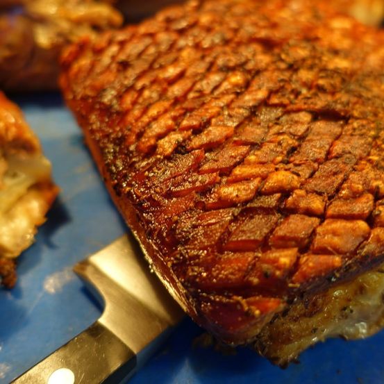 Ein Nahaufnahme von geschnittenem Schweinebauch mit knuspriger, goldbrauner Kruste, auf einer blauen Oberfläche.
