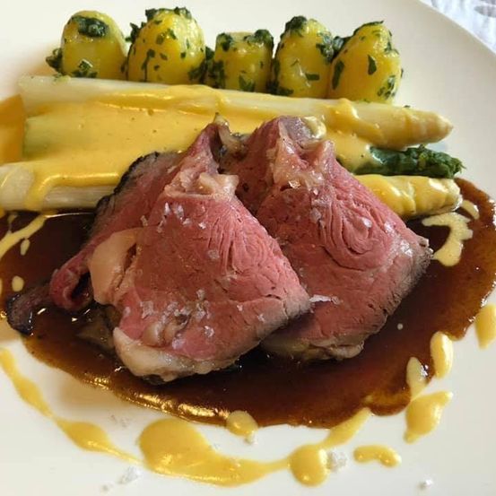 Ein Teller mit Steak, Spargel und Kartoffeln, überzogen mit brauner Soße und gelber Sahne.